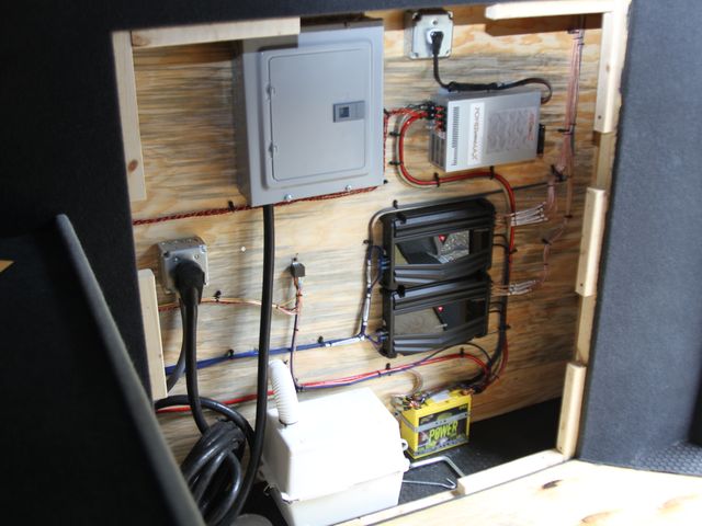 Electrical compartment during the build: breaker panel, power converter, amplifiers and battery wired onto the plywood wall