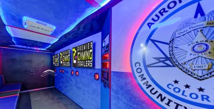 Inside the Five-O Activity Trailer: screens along the left wall, bench seating opposite, and the Aurora Police Community livery across the right-hand wall