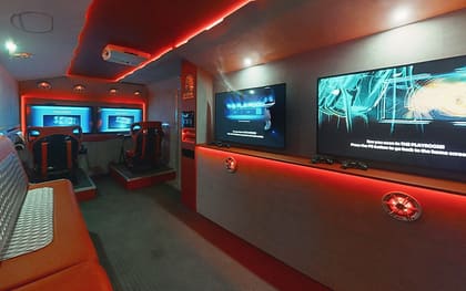 Inside a custom build: two racing simulator seats on raised platforms at the far end, red lit ceiling and counter, and screens along the right-hand wall