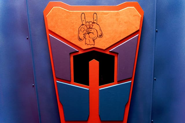 A carved ceiling panel in a converted gaming bus: an orange shape layered over purple and blue panels, with the owner's rock-hand logo engraved into it