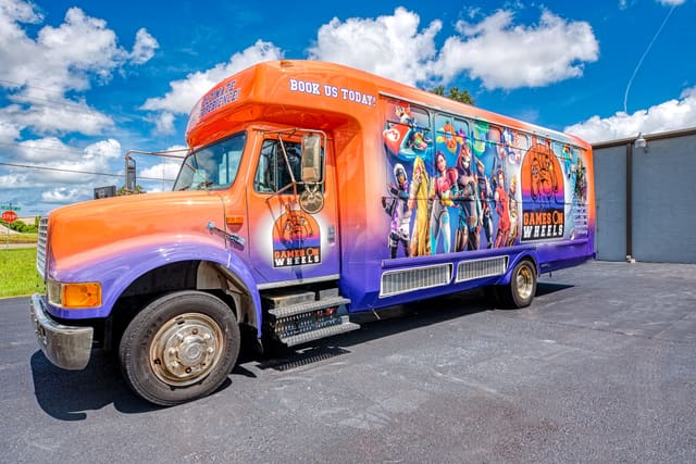 A converted gaming bus seen from the front corner, wrapped in the owner's branding with game artwork along the body, parked at a roadside