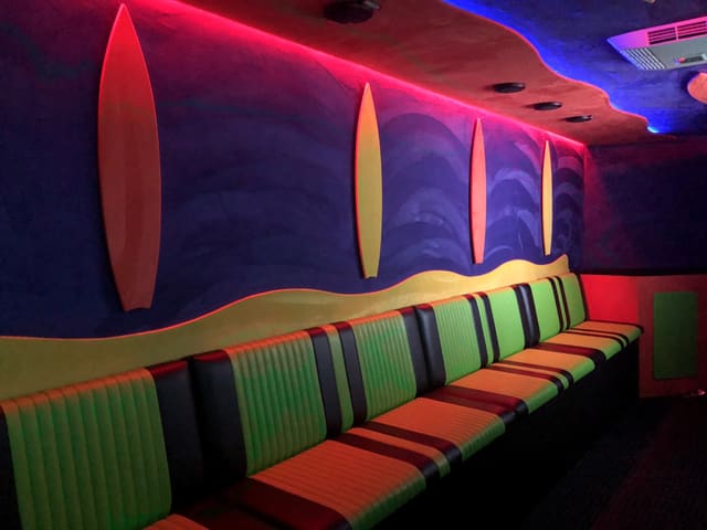 A channel-stitched bench in a Gamers Paradise, upholstered in green, orange and black stripes, along a wall painted with surfboards