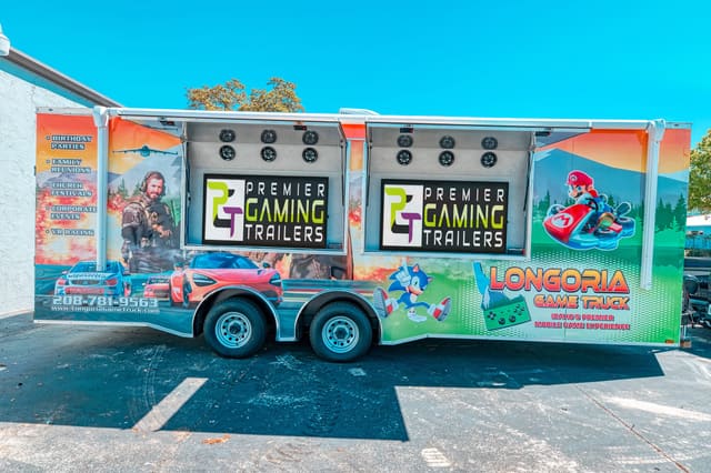 A Gamers Paradise from the side with two exterior screen hatches raised, a PGT screen under each and speakers mounted inside the hatches, and a full custom wrap along the body