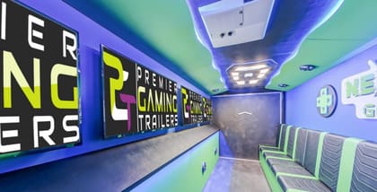 Inside the Level Up Gaming trailer: screens showing the PGT logo along the left wall, gray and green chevron-stitched benches down the right, and a lit ceiling feature