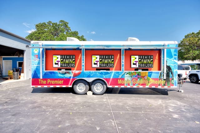 A Gamers Utopia from the side with all three exterior screen hatches raised, each screen showing the PGT logo, and a full custom wrap along the body