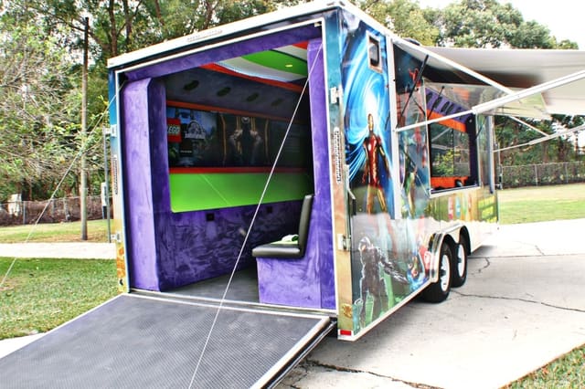 The same owner's gaming theater from the rear with the ramp down, showing the purple-lit interior and screens inside, with the awning out along the side