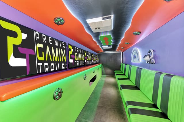 Inside a Gamers Utopia: lime green benches with black stripes on the right, PGT screens above an orange counter on the left, an orange ceiling lit with green LED, and a purple end wall with a lit emblem and a VR headset