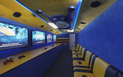 Inside a Gamers Utopia owner build: blue suede walls with a gold ceiling, screens along the left above a yellow counter, and yellow and navy striped benches on the right