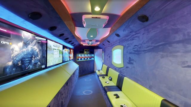 Opening view of the Gamers Utopia owner build tour: screens down the left wall above a lime bench, a black and lime bench with controllers on the right, purple suede walls and the lit console rack at the front