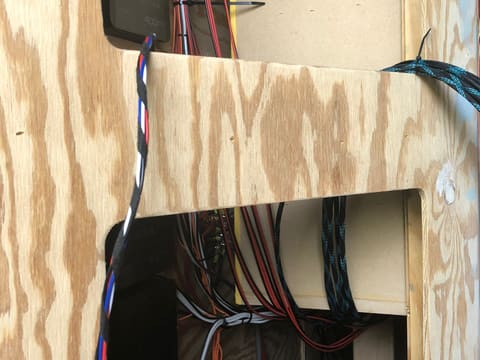 Wiring being run inside a gaming trailer's plywood wall frame: bundled speaker cable, zip ties and braided looms fed through the openings