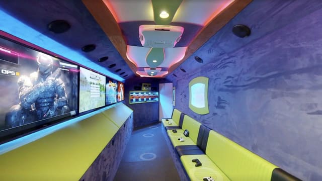 Inside a Gamers Utopia gaming theater: a run of wall-mounted screens over a lime bench on the left, purple suede walls, a black and lime bench on the right, and the lit console rack at the far end