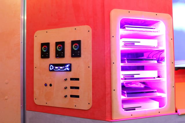 The control panel in a Mini Adventurer: three lighting controllers and a radio on a wall panel, beside an open cubby holding consoles on lit shelves