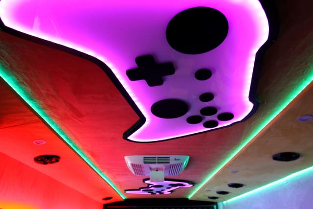 The ceiling of a Mini Adventurer: a game controller shape cut into the ceiling and lit from behind in purple, with an air conditioning unit beside it