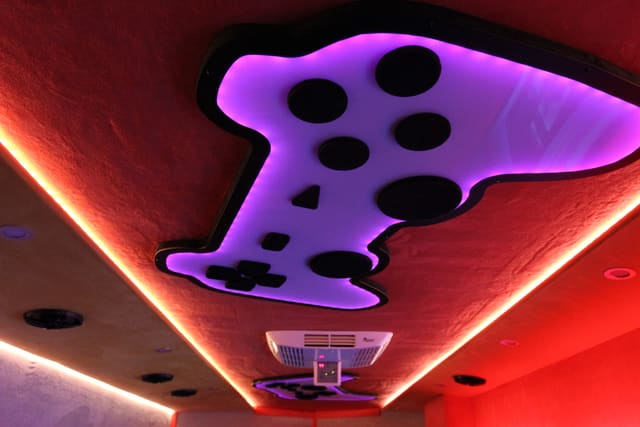 The ceiling of a Mini Adventurer: a game controller shape lit in purple and white, red LED light tracing the edge of the ceiling, and a projector hanging below it