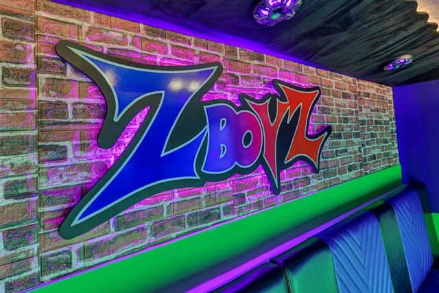 Inside a Mini Adventurer: a neon graffiti logo sign lit in blue and pink on a brick wall, above a lit green ledge and a quilted bench