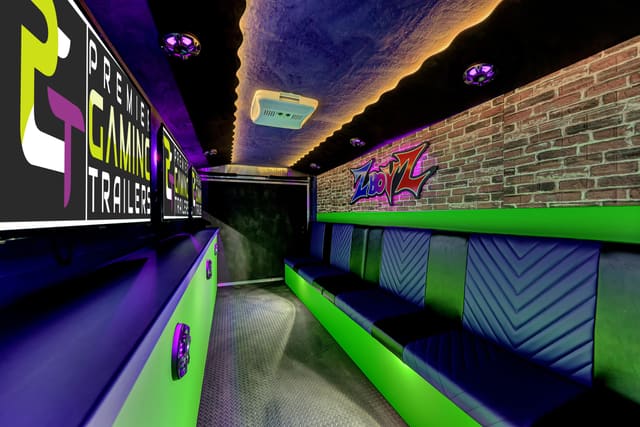 Looking down the length of a Mini Adventurer: PGT screens above a purple and green counter on the left, a brick wall with a lit logo sign and a quilted bench with a green base on the right, and a ceiling edged with warm LED light