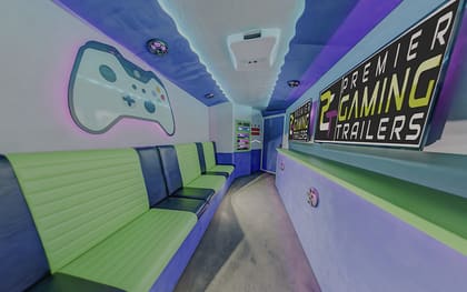Inside the Roving Leaders trailer: a large Xbox controller graphic lit on the left wall, a run of lime green benches beneath it, and PGT screens along the right