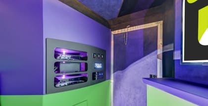 Inside the Zboyz Gaming trailer: a gray console panel with consoles on purple-lit shelves, green and purple walls, and a counter running down the right
