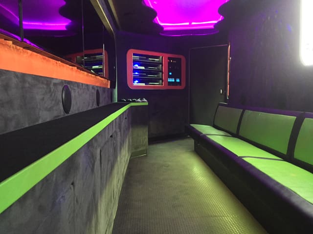 Interior of an earlier gaming trailer build: gray suede walls, a lime and black bench, a magenta ceiling glow and orange-framed console niches lit blue at the far end