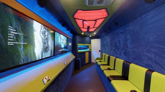 Interior of a finished gaming trailer: dark navy suede walls, a lime and black bench, a red glowing hexagonal ceiling feature and screens down the left wall