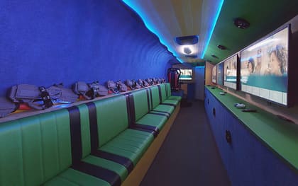 Inside a Virtual Reality owner build: green benches down the left with laser tag packs racked above them, and screens along the right under a blue lit ceiling