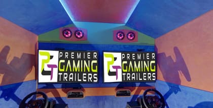 Inside the Ultimate Gaming Truck: two racing simulator rigs with steering wheels and pedals facing their own screens, under blue and orange walls
